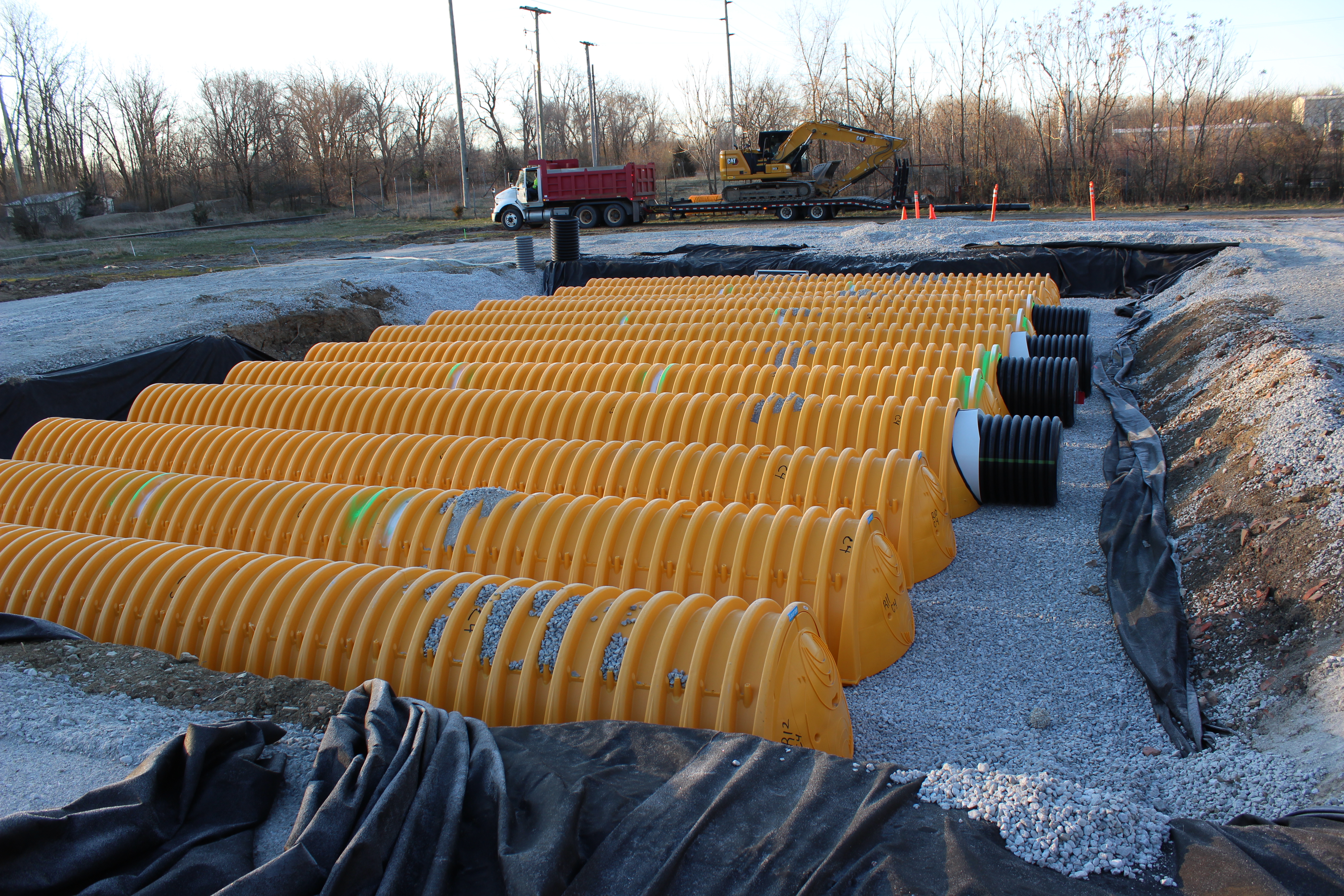 A large underground stormwater system installation featuring rows of bright yellow StormTech chambers partially embedded in gravel.